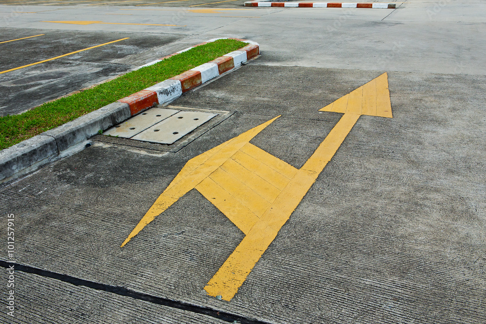 A yellow traffic arrow signage on an asphalt road indicating a d