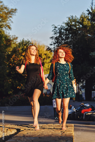 Girlfriends walking in the park barefoot.