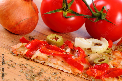 Vegetarian pizza, tomatoes onion and seasoning on wooden surface
