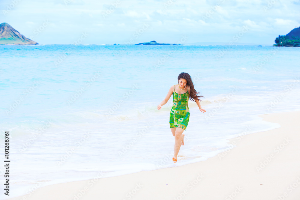 Beautiful teen girl in green dress running along Hawaiian beach