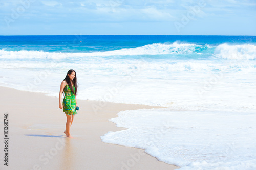 Beautiful teen girl in green dress walking along Hawaiian beach