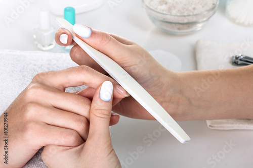 Closeup shot of a woman in a nail salon receiving a manicure by a beautician with nail file. Woman getting nail manicure. Beautician file nails to a customer. photo