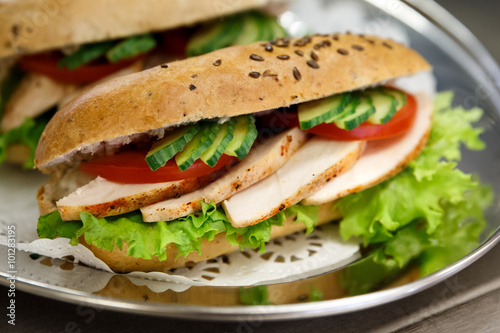 Sliced chicken or turkey and salad whole wheat filled baguettes on doily and stainless steel tray.