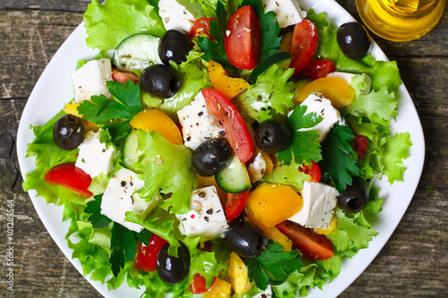 Greek salad with fresh vegetables, feta cheese and black olives on a wooden background