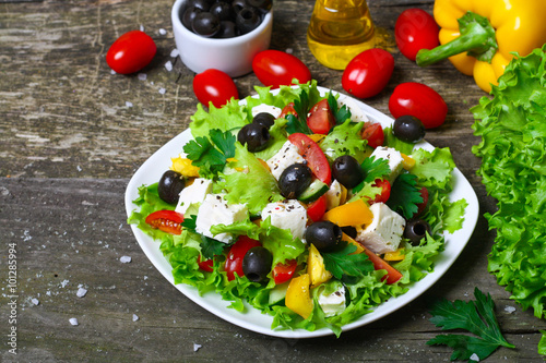 Greek salad with fresh vegetables, feta cheese and black olives on a wooden background