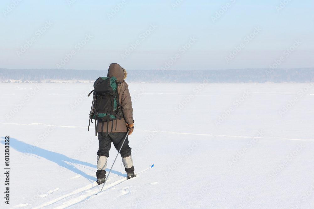 The man the traveler with a backpack skiing on snow of the frozen river
