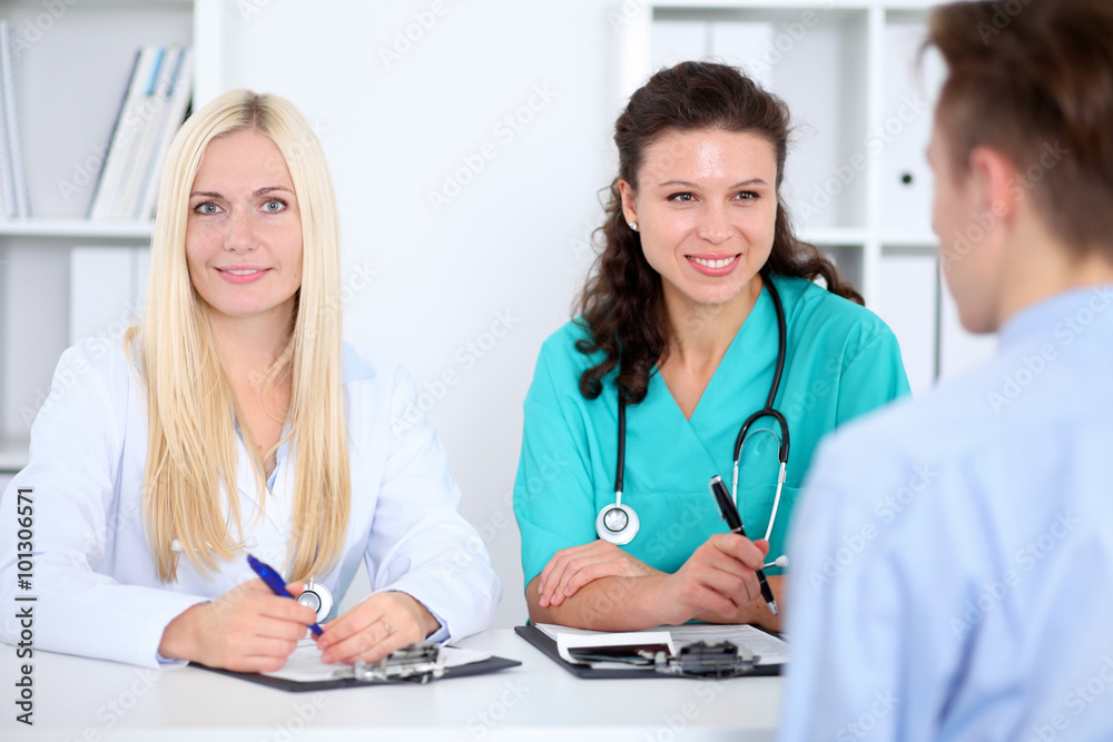Two confident friendly female doctors sitting at the table and listen to the patient's history . Medical and health care concept Two confident friendly female doctors sitting at the table and listen to the patient's history . Medical and health care concept