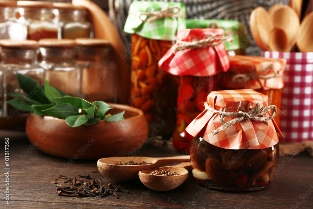 Jars with pickled vegetables, beans, spices and kitchenware on wooden background