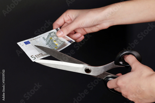Hands with scissors cutting Euro banknote, on black background