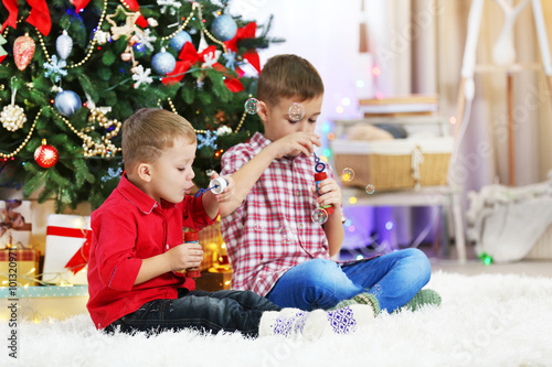 Two cute small brothers blows soap bubbles on Christmas tree background