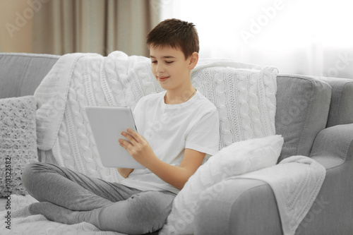 Boy using tablet on a sofa ...
