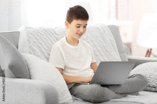 Boy using laptop on a sofa ...