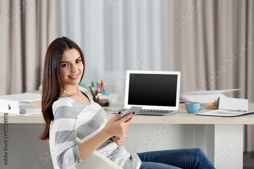 A beautiful young woman with a mobile phone working at home as a freelancer