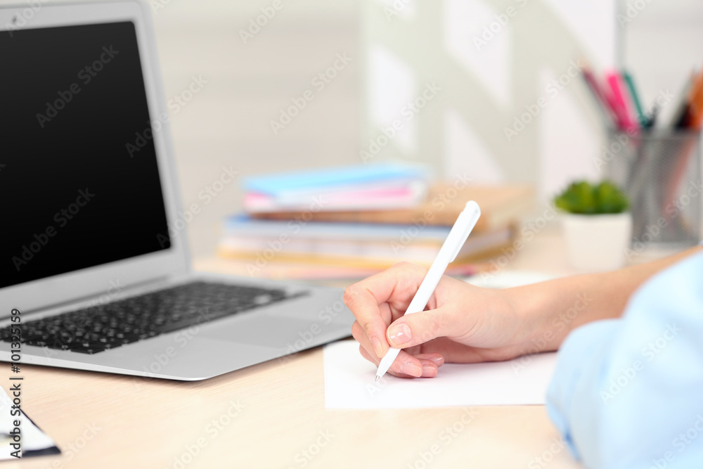 Woman making notes on a sheet of paper with a laptop beside Woman making notes on a sheet of paper with a laptop beside
