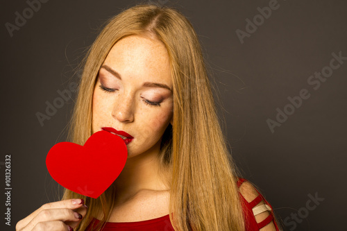  woman biting red heart, looking down. studio black background
