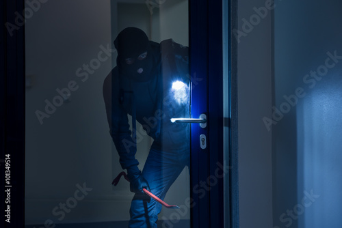 Fotografia Thief With Flashlight Trying To Break Door