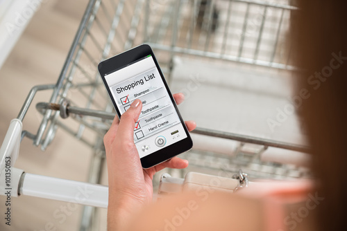 Woman Checking Shopping List On Smartphone In Supermarket