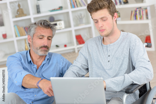 Man helping boy in wheelchair to use a computer