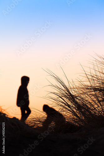 Silhouette Beach Scene / Silhouettes of a bunch of grass and two unrecognizable playing children as blurred background at evening light at the beach