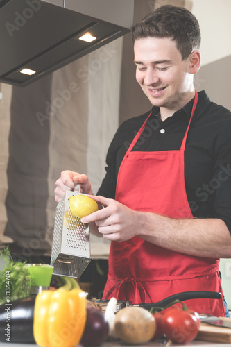 Junger Mann reibt Zitronenschale in die Bratpfanne