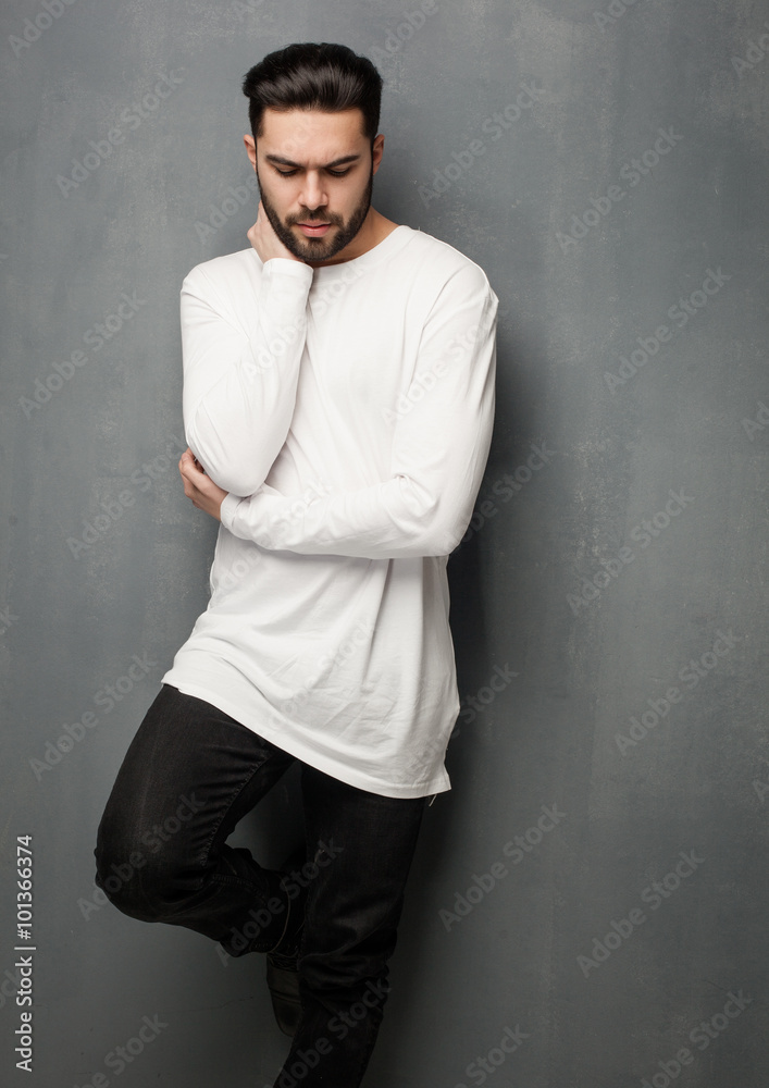 sexy fashion man model in white sweater, jeans and boots posing dramatic