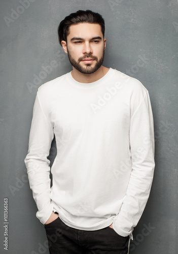 sexy fashion man model in white sweater, jeans and boots posing dramatic