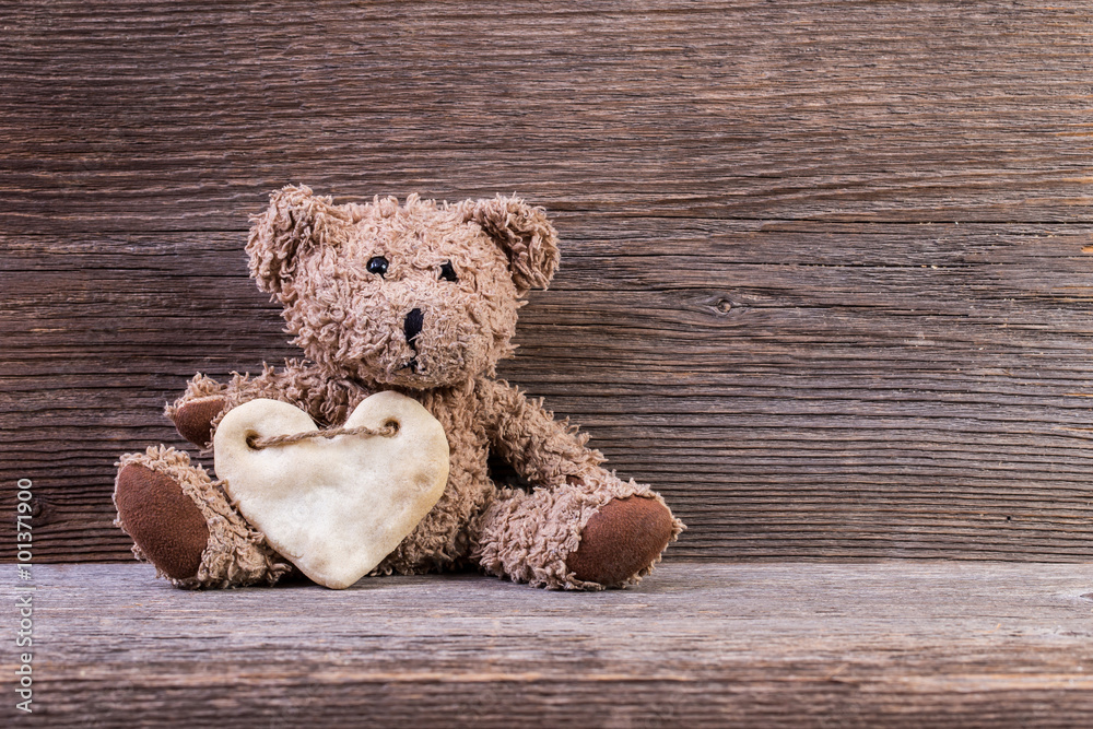Obraz premium Teddy bear with heart sitting on old wood background.