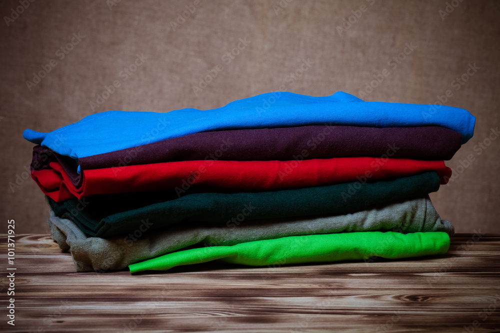 Stack of T-shirts on wooden table opposite a defocused burlap ba Stack of T-shirts on wooden table opposite a defocused burlap ba