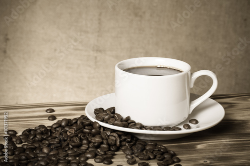 Coffee beans and coffee in white cup on wooden table opposite a