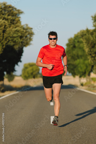 Fit man running on country road. Male athlete training outdoor for marathon and endurance.
