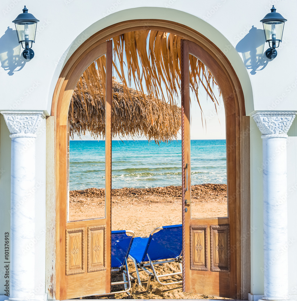 Fototapeta Widok przez otwarte drzwi na morze, plażę z niebieskimi leżakami