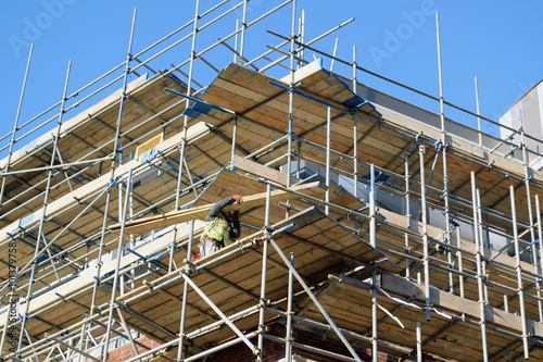 Large scaffolding on a building with worker holding wooden board © Savo Ilic