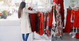 Young woman looking for a colorful red dress searching through garments hanging on a rail outside a shop in an urban street