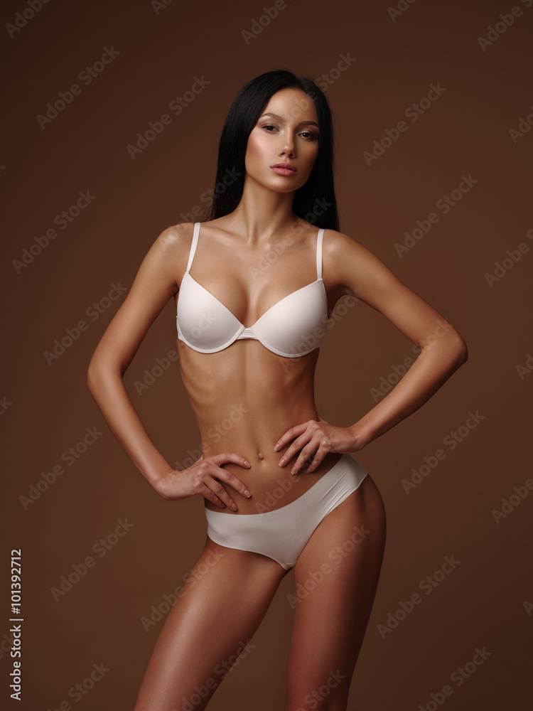 Young skinny model with black straight hair is posing in the white basic seamless underwear collection in the studio