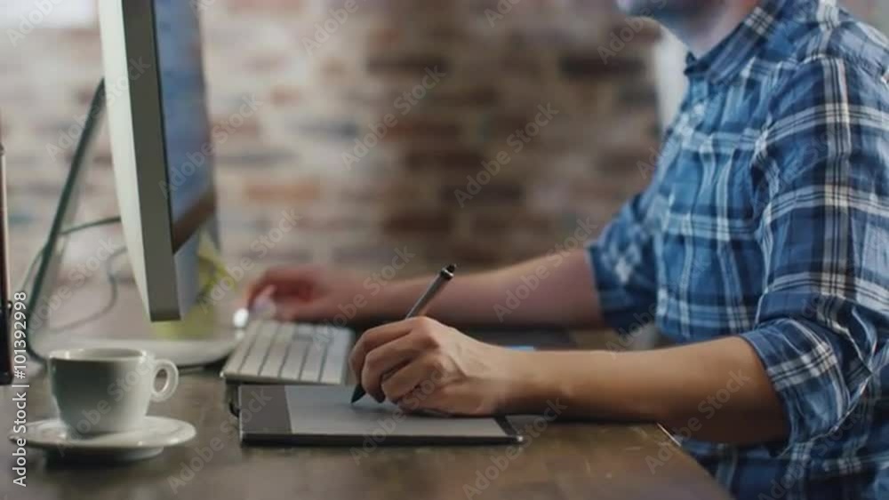 Young designer sitting in front of a monitor in a loft and sketching on a graphic tablet. Shot on RED Cinema Camera.