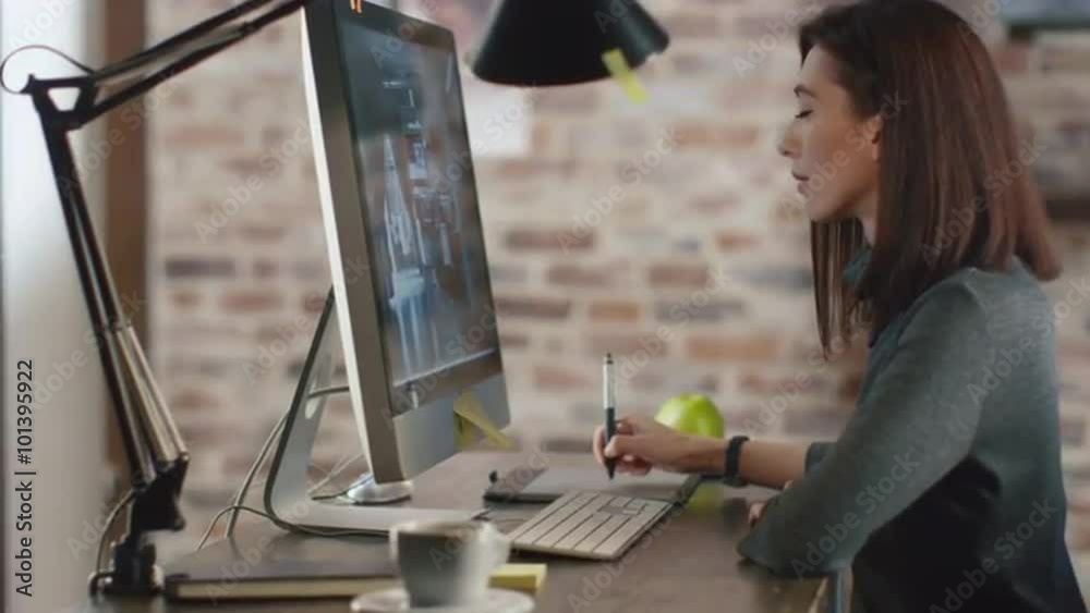 Young brunette woman is editing pictures with a graphic tablet on a computer. Shot on RED Cinema Camera.