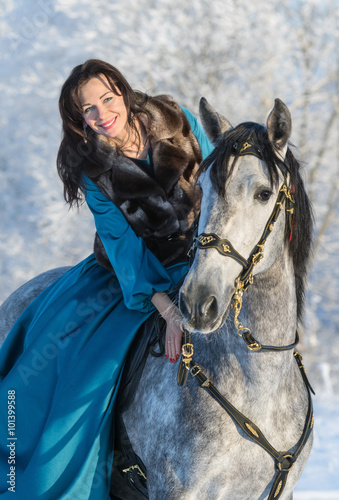 Woman in a blue dress riding on a grey stallion