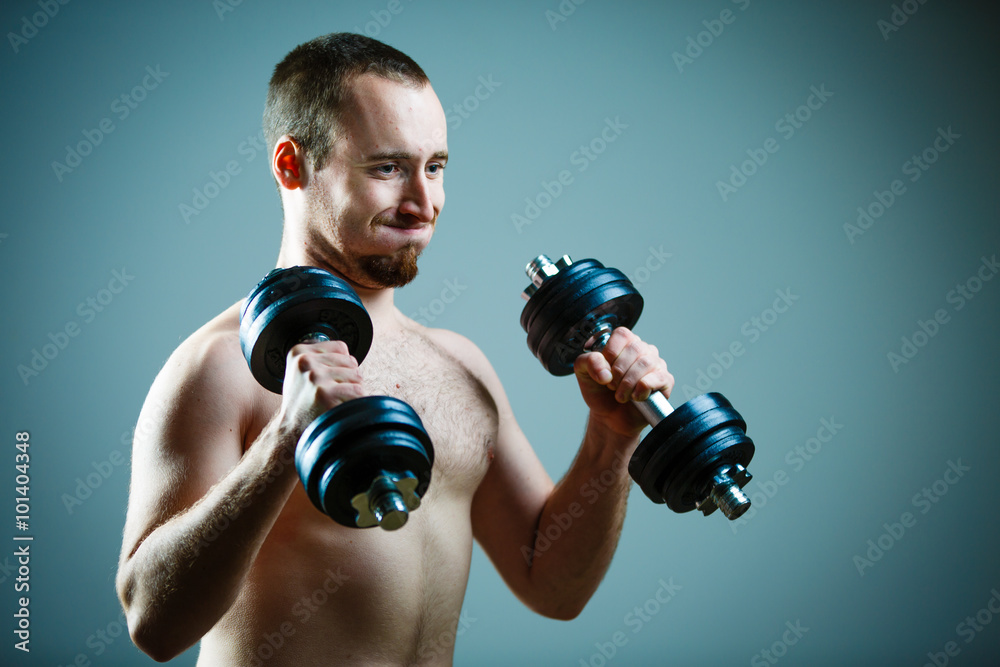Close up of young man lifting weights over grey background Close up of young man lifting weights over grey background