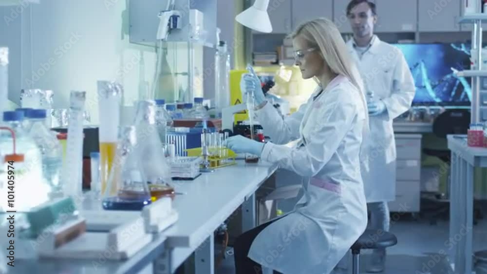  Female scientist is using a micro pipette while working in a laboratory with colleagues. Shot on RED Cinema Camera.