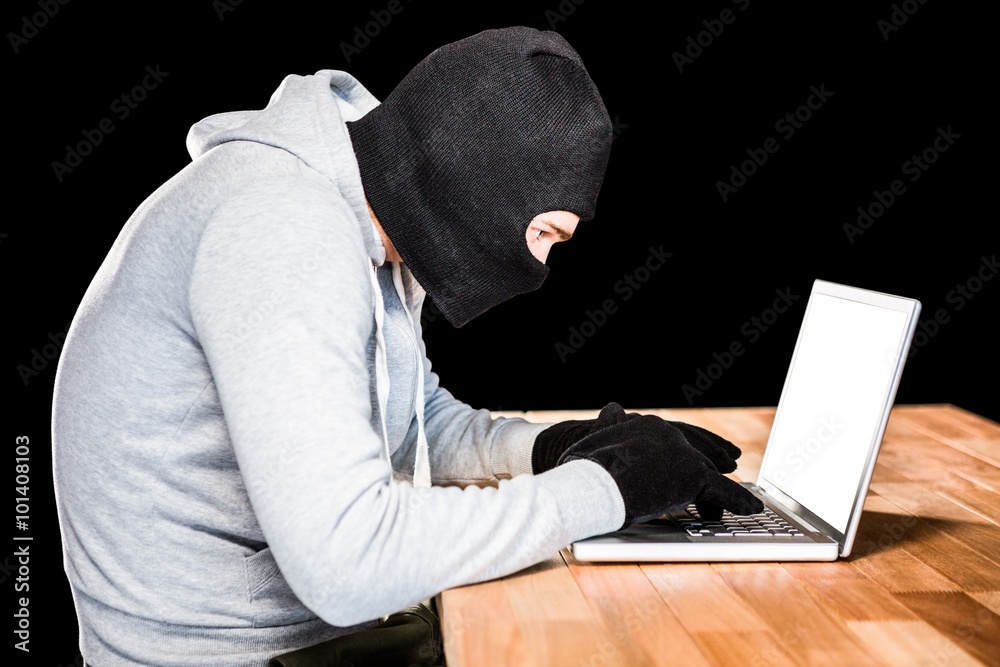 Focused thief with hood typing on laptop Focused thief with hood typing on laptop