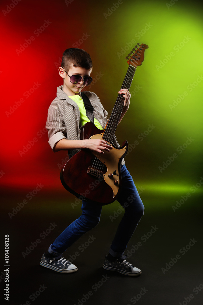Fototapeta premium Little boy playing guitar on a bright background