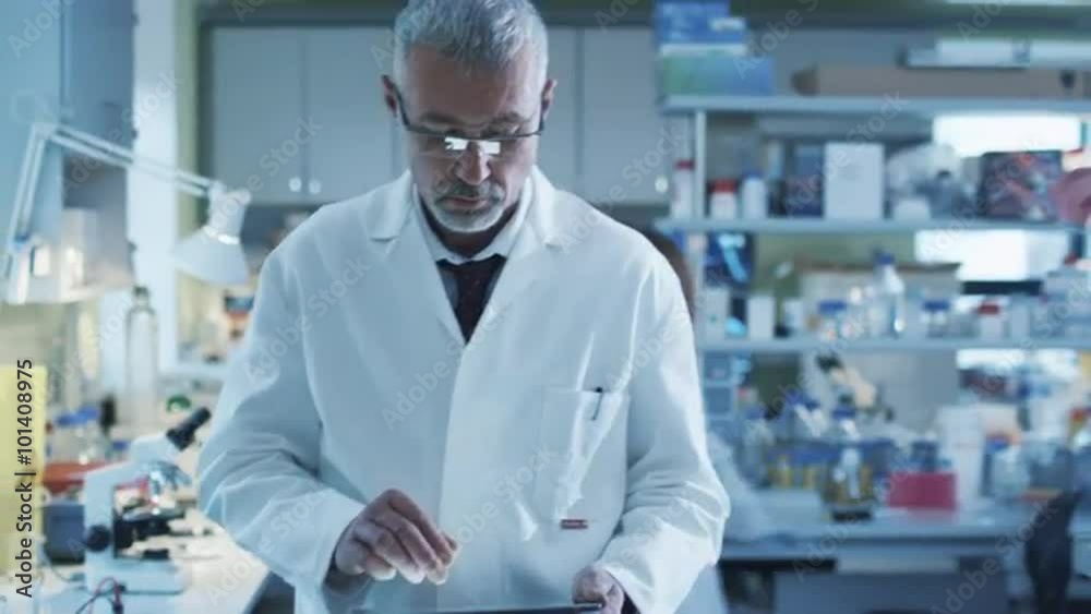 Senior scientist is walking with a tablet in a laboratory where colleagues are working. Shot on RED Cinema Camera. Senior scientist is walking with a tablet in a laboratory where colleagues are working. Shot on RED Cinema Camera.