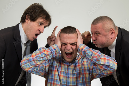 Young man being yelled at by two senior male manager on white