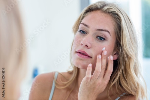 Smiling pretty woman applying cream on her face