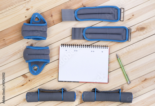 Sport Equipment. Dumbbells, Ankle Weights, Wrist Weights And Notebook To Workout Plan On Boards. Sport Fitness Background