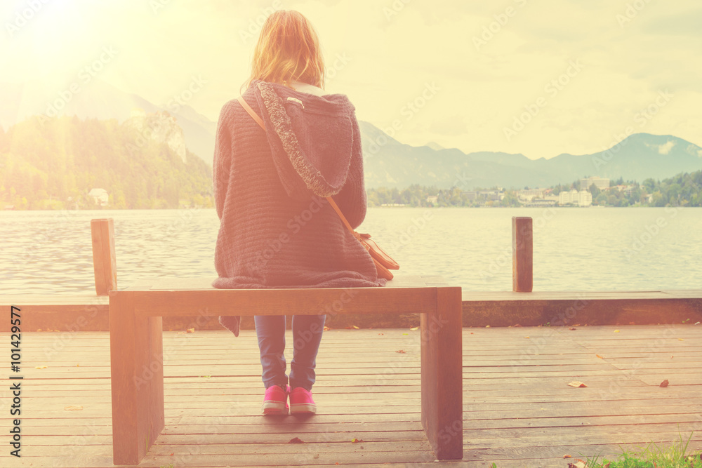 Girl sitting on a wooden pier near water.