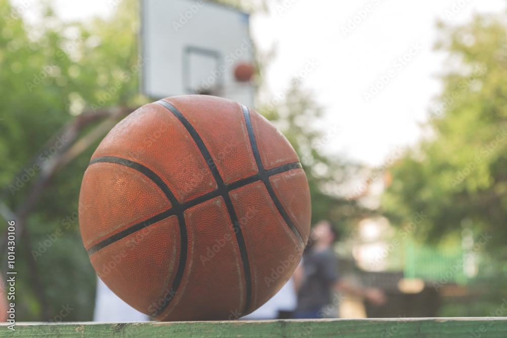 Basketball ball on a bench with defocused players in the background. Basketball ball on a bench with defocused players in the background.