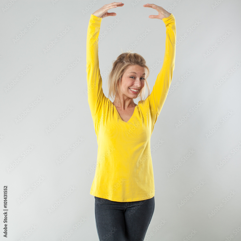 Φωτογραφία success concept - smiling 20s blond woman with yellow shirt dancing with graceful hands up for happiness or vitality,studio shot