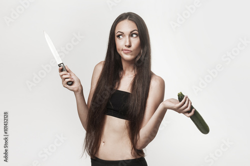 Funny image of young woman holding zucchini and knife