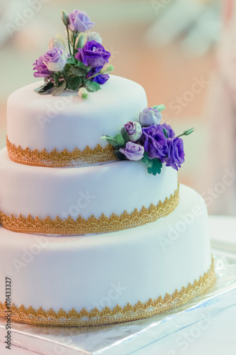 The white wedding cake, decorated with the soil gold and violet floral. Selective focus.